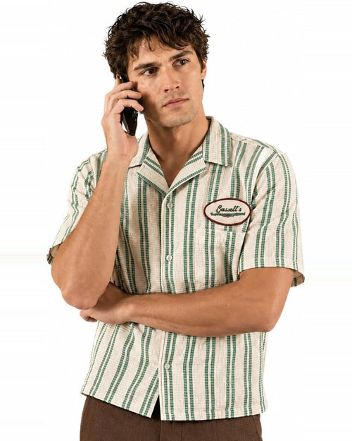 Green and cream striped camp shirt worn with a phone to the ear